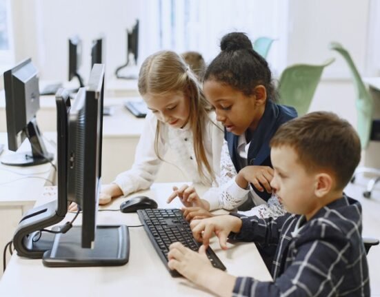 Três crianças, duas garotas e um menino, mexendo no computador em um laboratório de informtática.