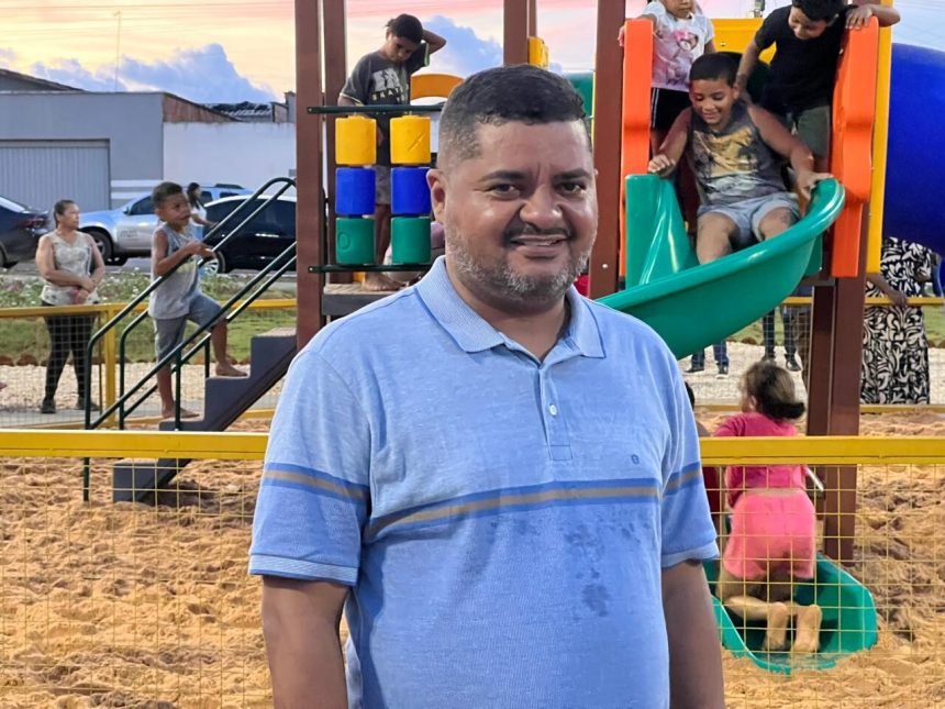 Veraedor Balaio sorrindo para a câmera. Ao fundo, crianças brincando no escorregador. Cenário: praça.